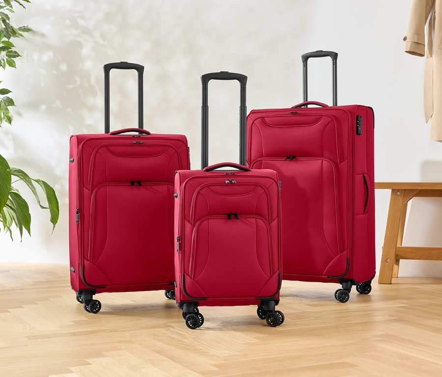 Trois valises rouges à roulettes de différentes tailles sont posées sur un parquet, à côté d'une plante et d'un banc.