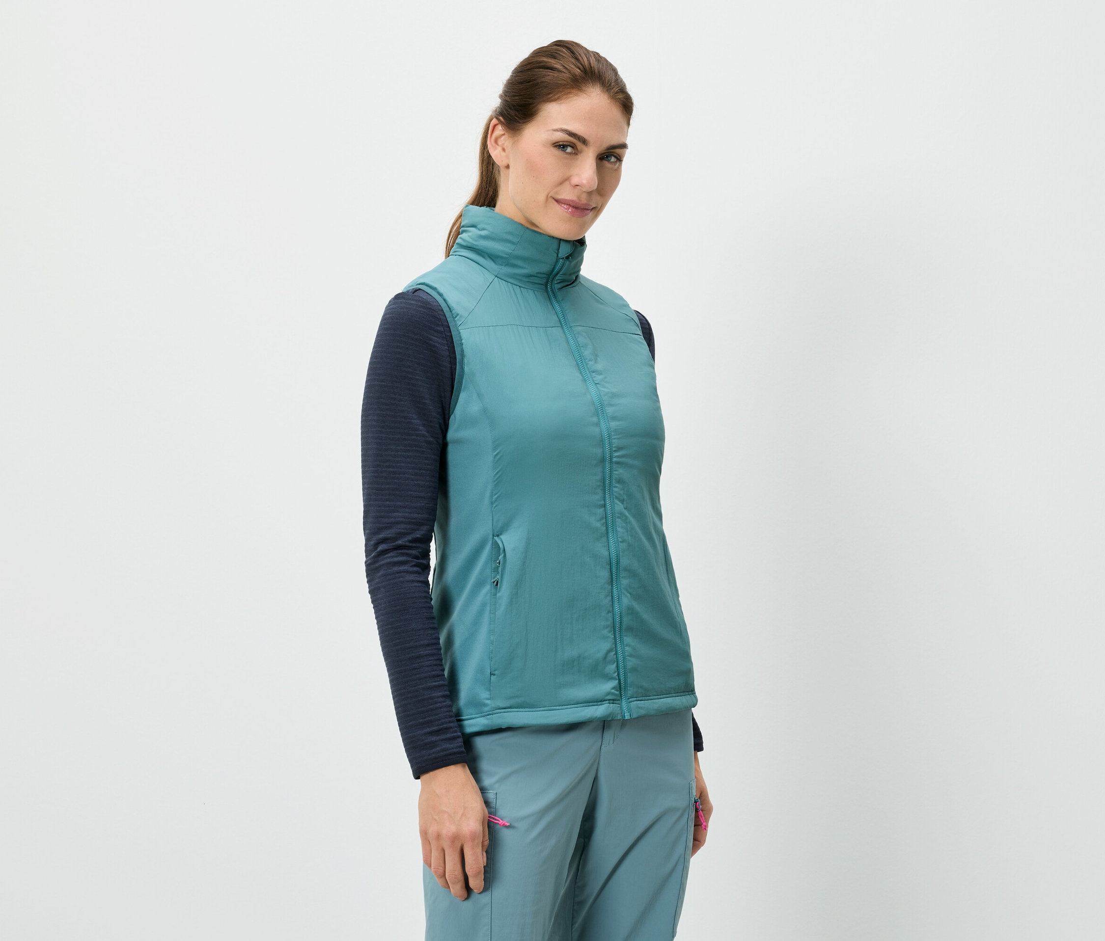 Une femme se tient debout et porte une veste bleue sur un haut à manches longues, associée à un pantalon bleu.