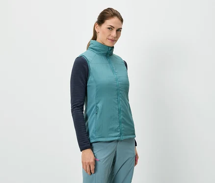 Une femme se tient debout et porte une veste bleue sur un haut à manches longues, associée à un pantalon bleu.