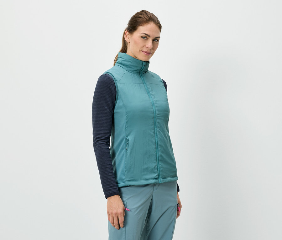 Une femme se tient debout et porte une veste bleue sur un haut à manches longues, associée à un pantalon bleu.