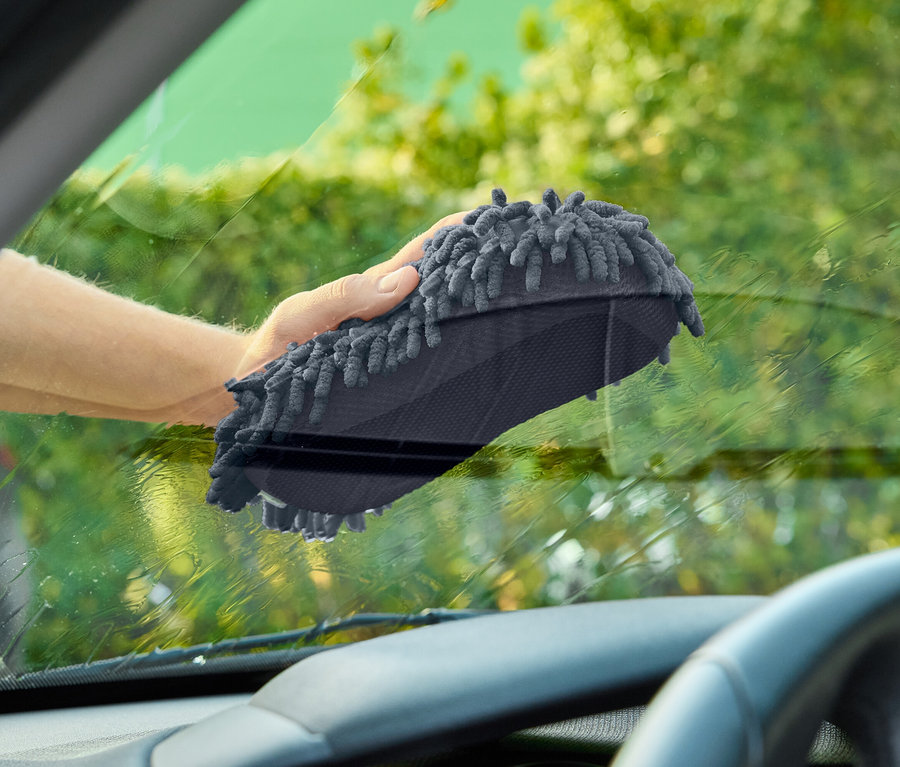 Une main essuie le pare-brise d'une voiture avec un gant de toilette gris.