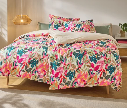 Lit avec literie à motifs de feuilles et d'oiseaux. Des décorations et des livres sont posés sur la table de chevet.