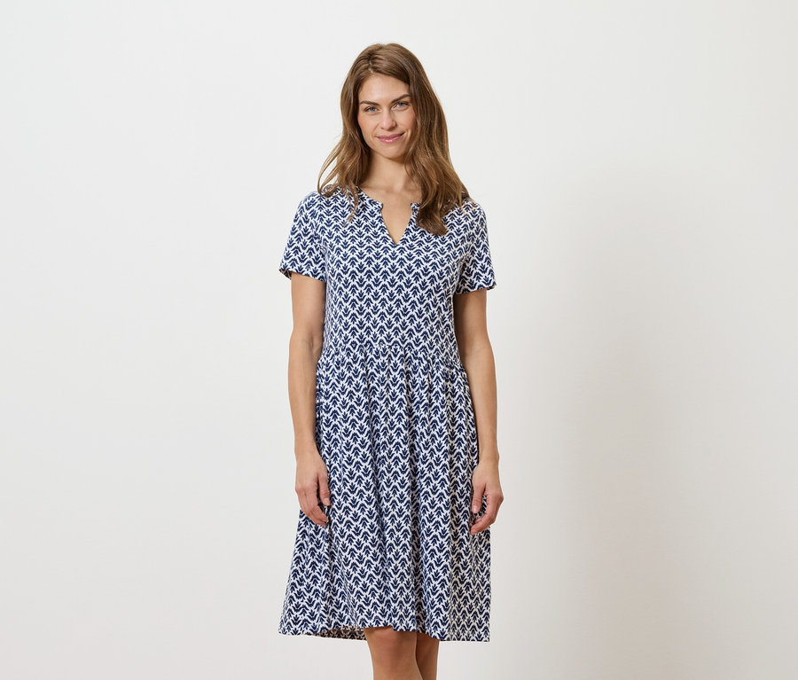 Femme debout portant une robe bleue et blanche.