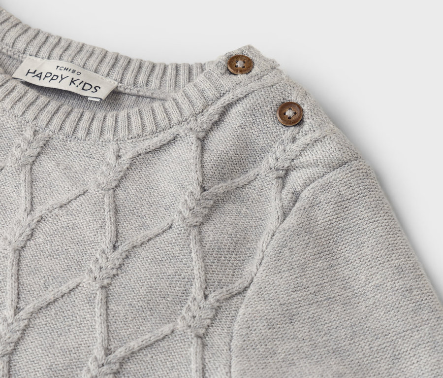 Gros plan sur un pull en tricot gris clair avec un motif torsadé et deux boutons sur l'épaule.
