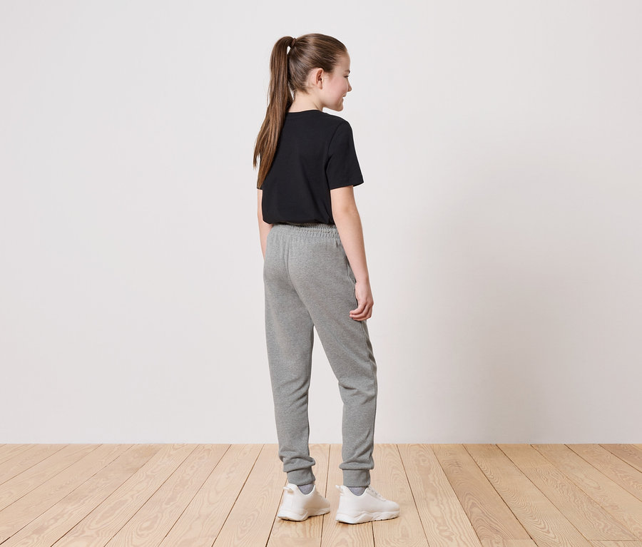 Une fille avec une queue de cheval porte un t-shirt noir, un jogging gris et des baskets blanches.