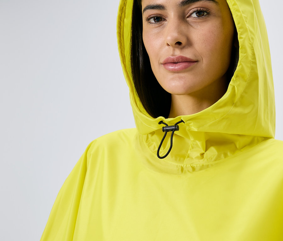 Une femme à capuche porte un poncho de pluie jaune avec cordon de serrage.