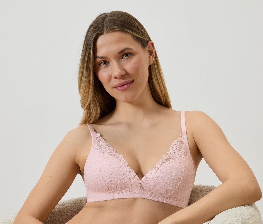 Une femme est assise dans un fauteuil et porte un soutien-gorge en dentelle rose clair.