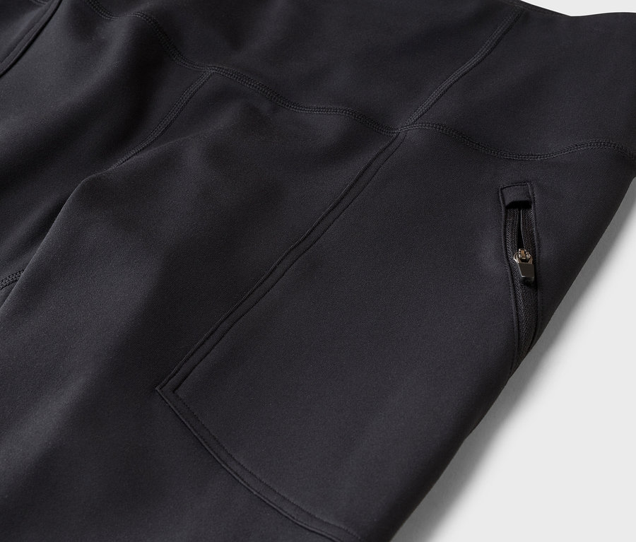 Gros plan d'un legging ou pantalon de sport noir, avec une poche latérale zippée et des coutures apparentes.