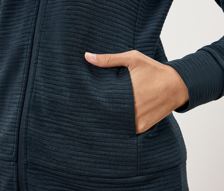 Gros plan d'une personne portant une veste texturée bleu foncé et mettant sa main dans une poche de veste.
