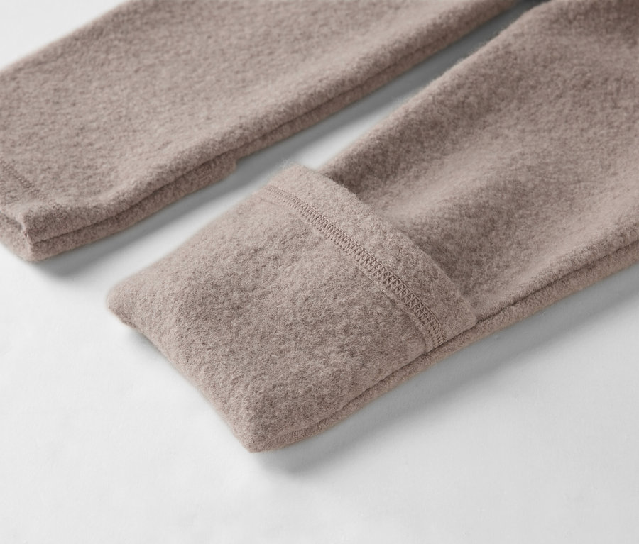 Gros plan sur deux manches d'un pull en laine marron clair sur fond blanc.