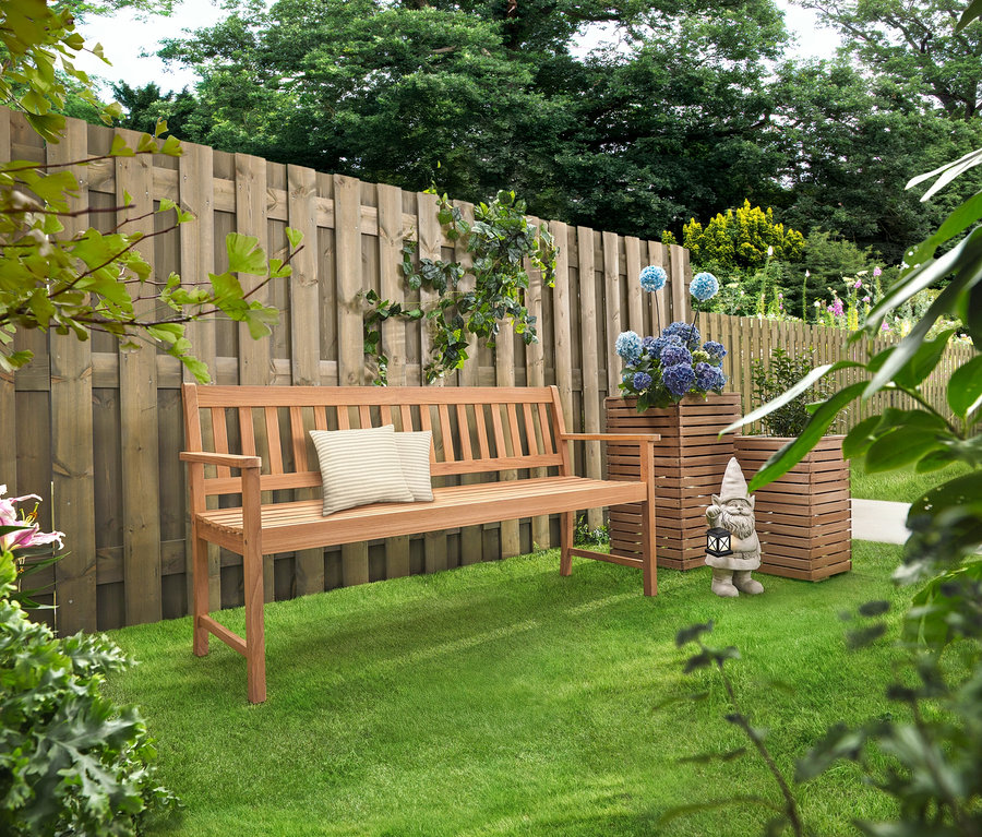 Un banc en bois avec des coussins se trouve sur une pelouse. Derrière se trouvent deux colonnes de plantation »Tinus« avec des fleurs bleues.