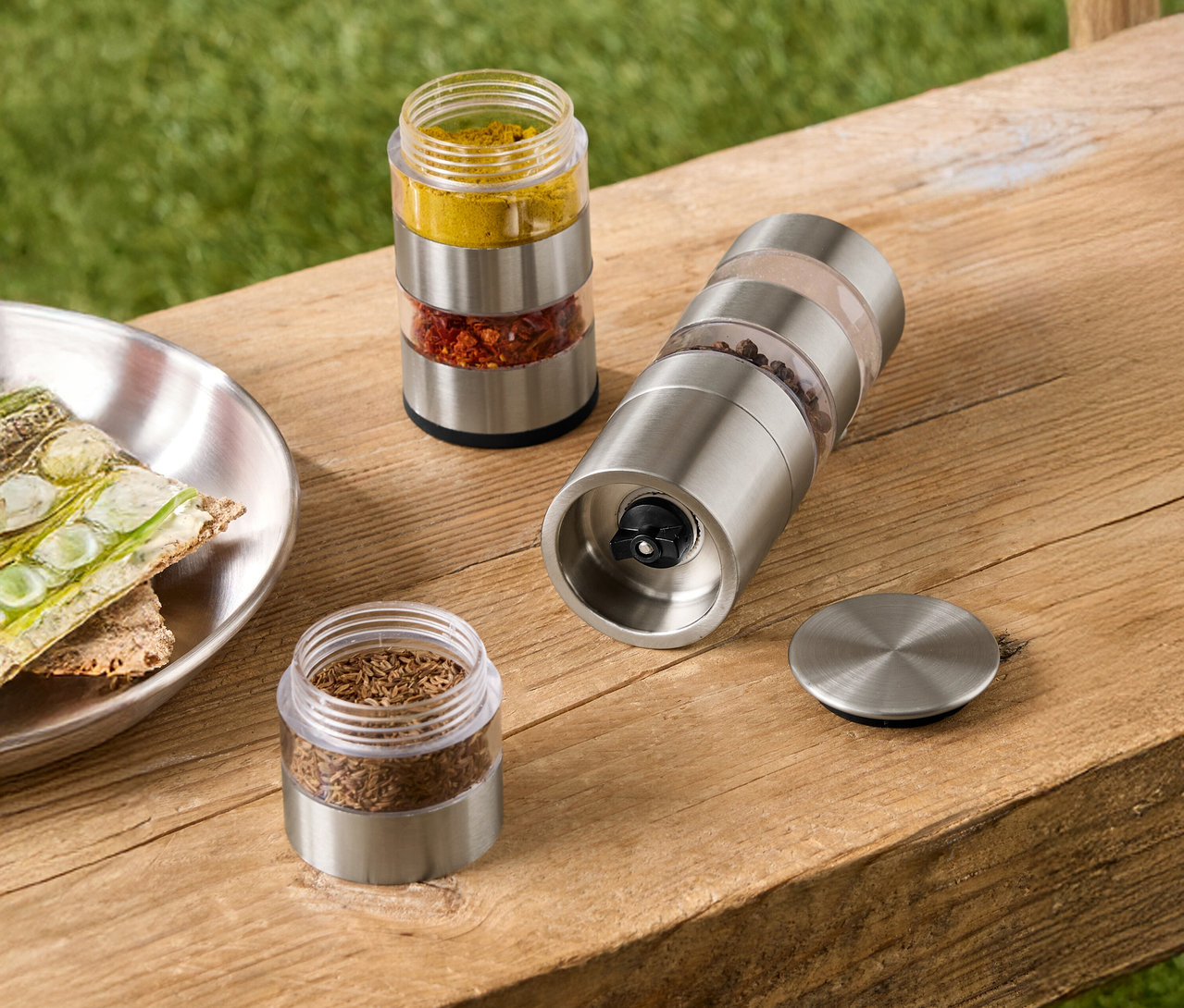 Sur un banc en bois se trouvent des récipients à épices contenant du curcuma, du piment et du cumin, ainsi qu'un moulin à épices contenant du poivre et du sel.