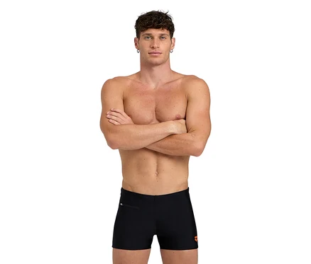 Homme les bras croisés, vêtu d'un short de bain noir.