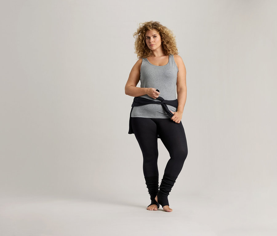 Femme aux cheveux bouclés portant un débardeur gris et un legging noir.