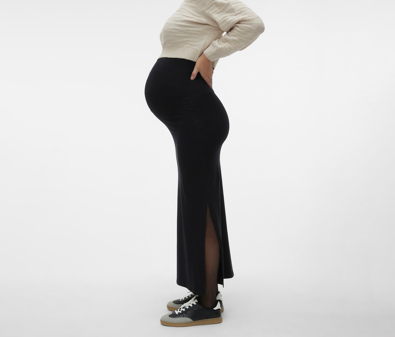 Femme enceinte portant un pull beige et une jupe maxi noire MAMALICIOUS «
MLEMMA TUBE
» avec fente et baskets.