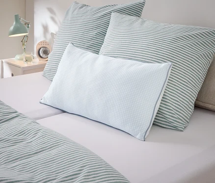 Gros plan d'oreillers et de linge de lit à rayures blanches et vertes sur un lit.