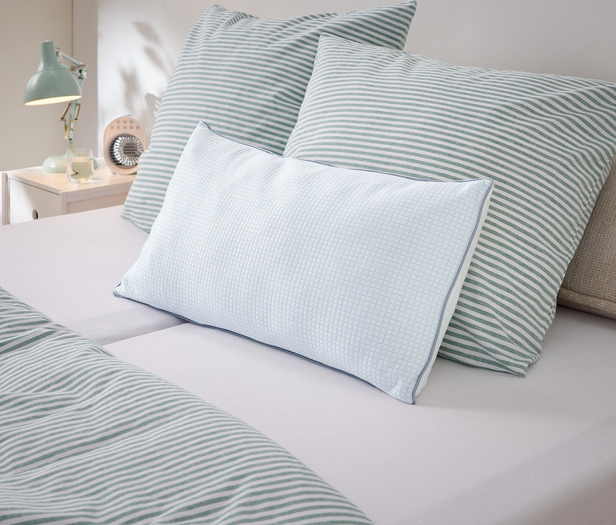 Gros plan d'oreillers et de linge de lit à rayures blanches et vertes sur un lit.