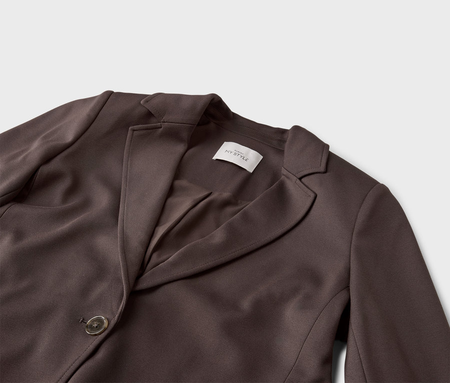 Gros plan d'un blazer marron avec bouton et revers sur fond gris.