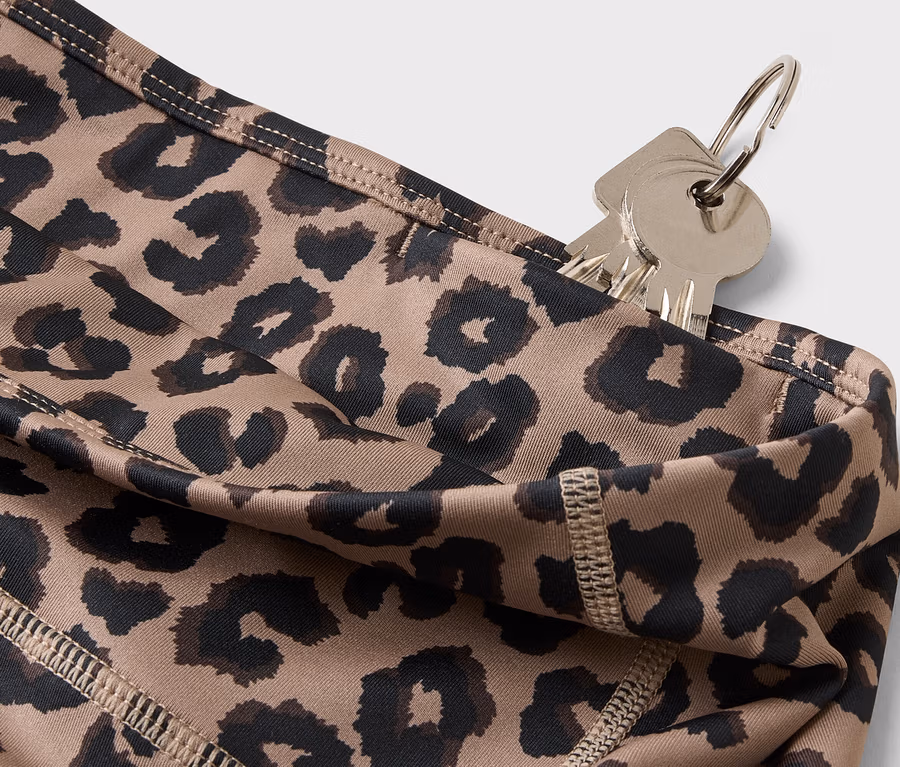 Gros plan de clés suspendues à un porte-clés glissées dans la poche d'un legging à motif léopard.