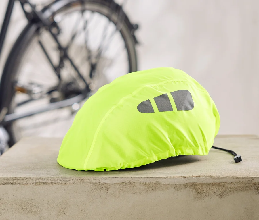 Une housse de casque de vélo jaune fluo avec des bandes réfléchissantes repose sur un socle en béton, avec un vélo en arrière-plan.