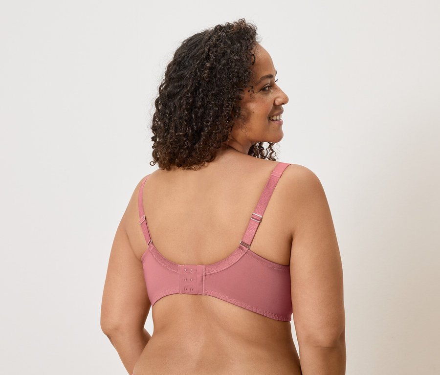 Vue arrière d'une femme aux cheveux bouclés portant un soutien-gorge rose avec des bretelles réglables et une fermeture à agrafes.