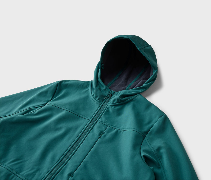 Gros plan d'une veste à capuche turquoise zippée, posée sur une surface blanche. La capuche est doublée d'un tissu plus foncé.