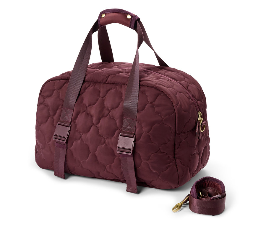 Un sac de voyage bordeaux matelassé avec des poignées et une bandoulière est posé sur un fond blanc.