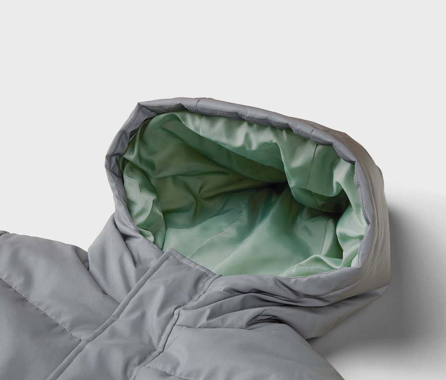 Gros plan d'un manteau en duvet gris avec une capuche dont l'intérieur est vert clair.