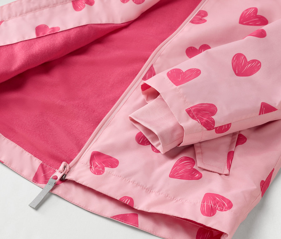 Gros plan d'une veste enfant rose clair ouverte, ornée de motifs de cœurs rouges et dotée d'une fermeture éclair intégrale.