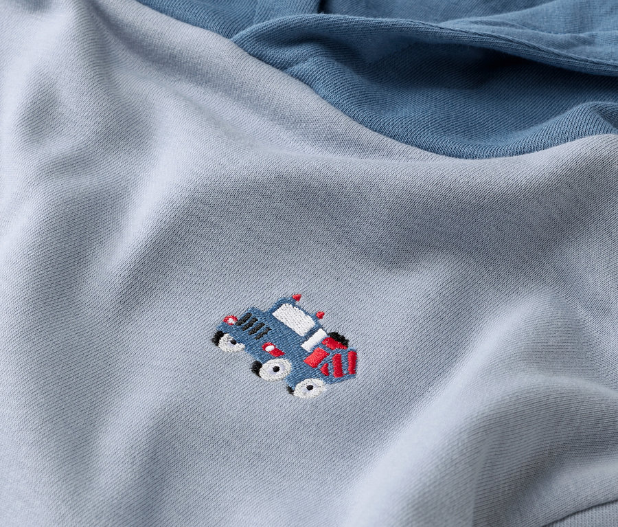 Gros plan d'un sweat-shirt bleu clair avec une manche bleu foncé et un appliqué de voiture bleue.