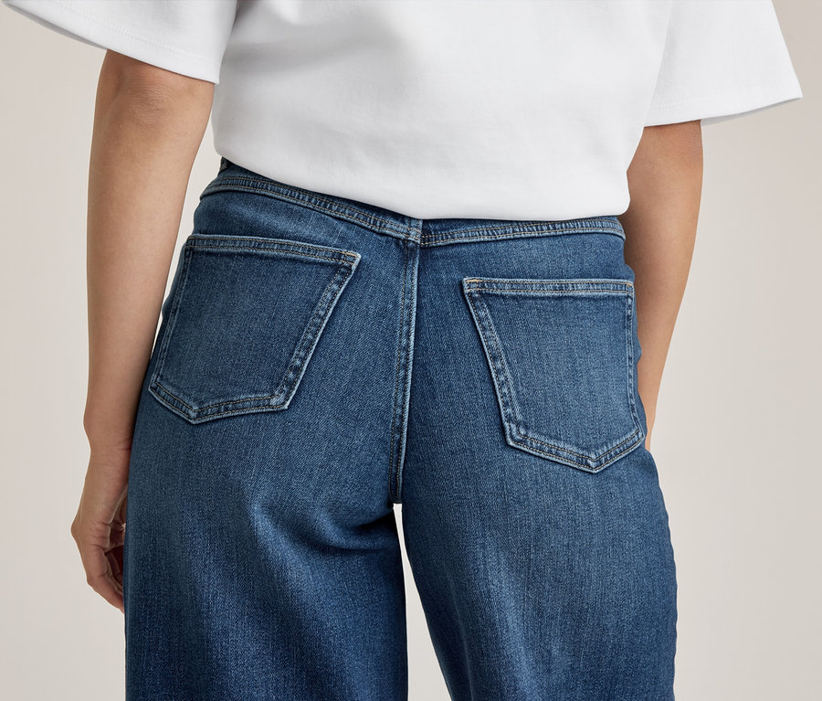 Vue de dos d'une personne portant un jean en denim bleu avec deux poches arrière et un t-shirt blanc.