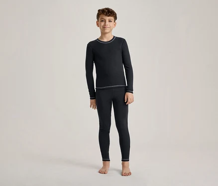 Un garçon se tient pieds nus, vêtu d'un t-shirt à manches longues bleu foncé et d'un legging assorti avec des coutures claires.
