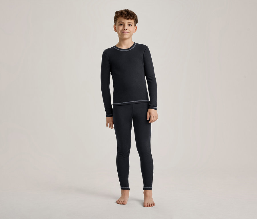 Un garçon se tient pieds nus, vêtu d'un t-shirt à manches longues bleu foncé et d'un legging assorti avec des coutures claires.