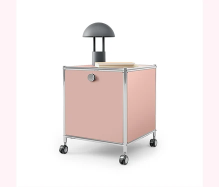 Un caisson rose à roulettes avec un cadre chromé et une lampe grise dessus.