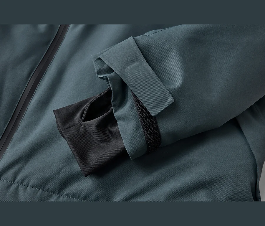Manche de veste vert pétrole avec fermeture éclair noire, sangle auto-agrippante réglable et poignet intérieur avec trou pour le pouce.