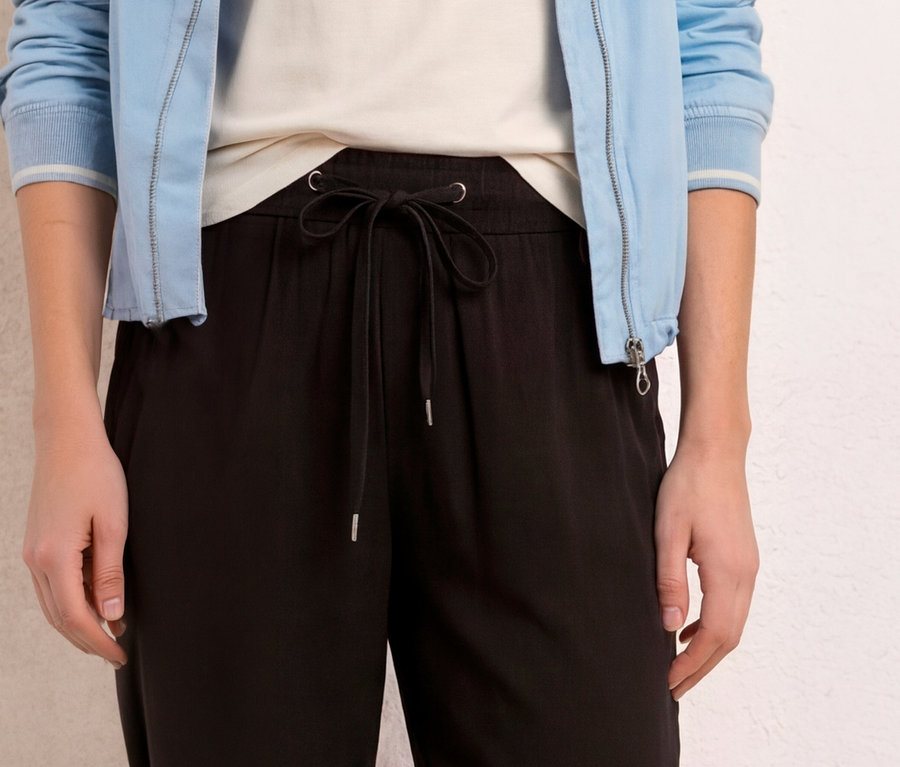 Une personne porte un culotte 7/8 Street One « EMMA » noir avec un cordon de serrage noué, un haut blanc et une veste bleu clair.