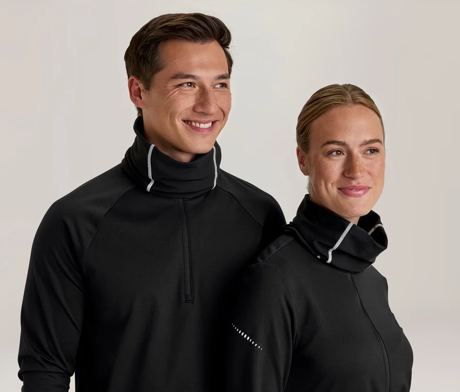 Homme et femme souriants portant des hauts noirs à manches longues avec col montant et liseré blanc. Le haut de l'homme a un quart de zip, et les deux ont des points réfléchissants sur les manches.