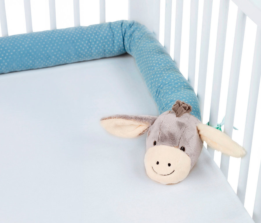 Un tour de lit bleu à pois avec une tête d'âne en peluche, posé dans un lit de bébé blanc avec un drap bleu clair.