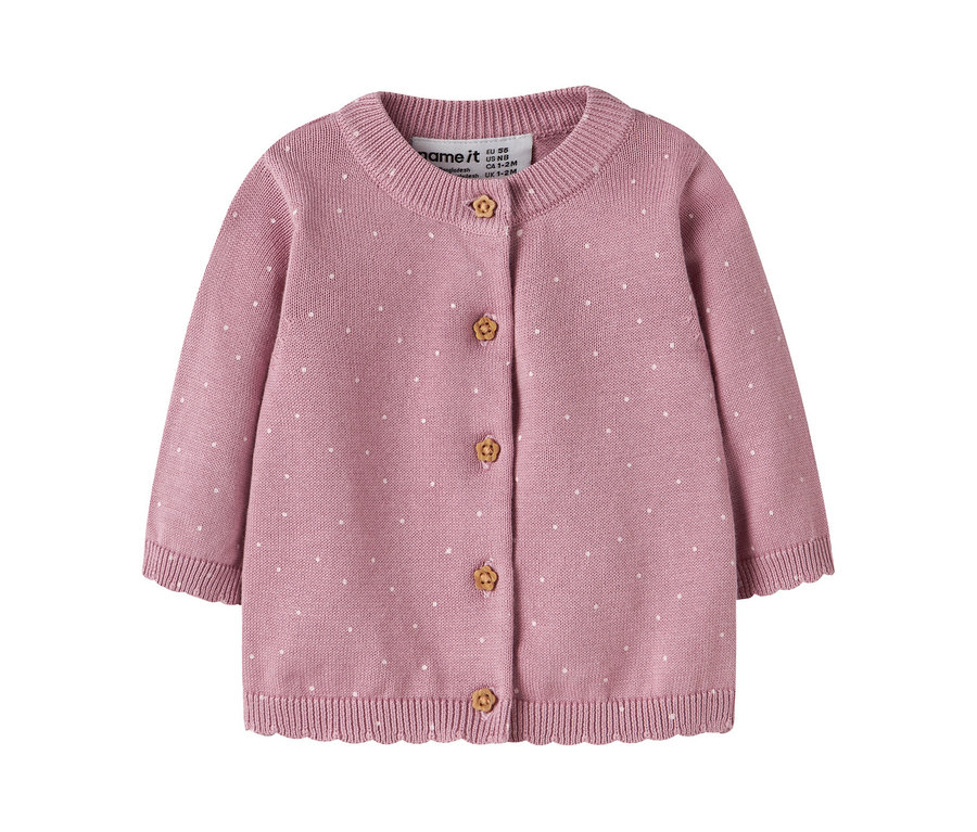 Cardigan bébé en tricot rose à pois blancs, col rond et manches longues. Il présente cinq boutons marron clair sculptés de fleurs et un ourlet côtelé festonné. Une étiquette de marque "name it" est visible.