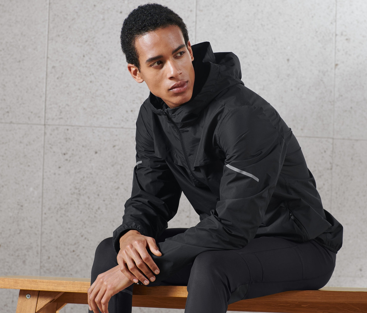 Homme assis sur un banc portant une veste coupe-vent noire.