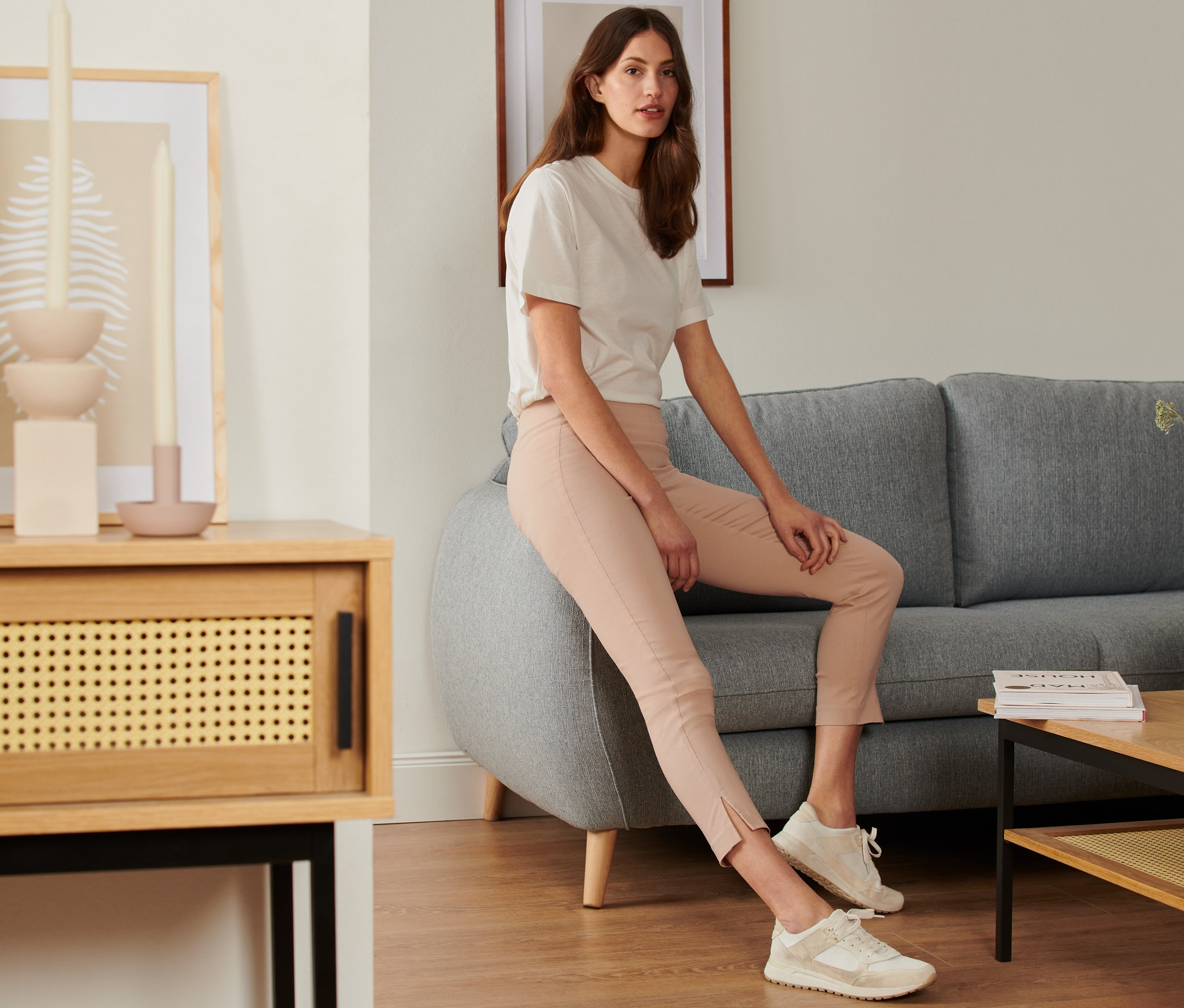 Une femme est assise sur un canapé gris et porte un pantalon stretch.