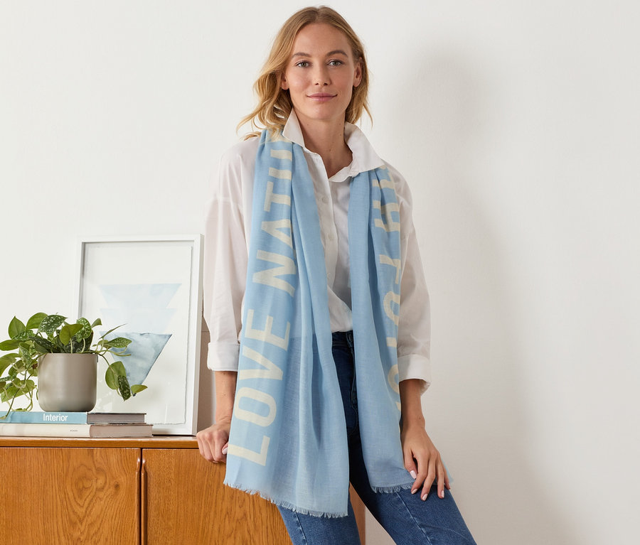 Une femme s'appuie contre une armoire et porte une écharpe tissée avec inscription imprimée.