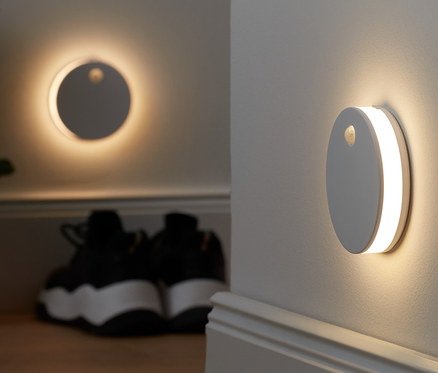 Deux éclairages multifonction à LED sont fixés au mur. À l'arrière-plan, il y a une plante en pot et des chaussures.