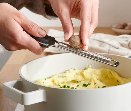 Femme râpant de la noix de muscade avec une râpe à muscade au-dessus d'une casserole de purée.