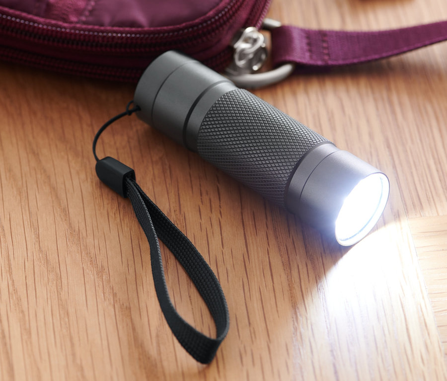 Une lampe de poche à LED allumée repose sur un plancher en bois à côté d'un sac à main bordeaux et de clés.