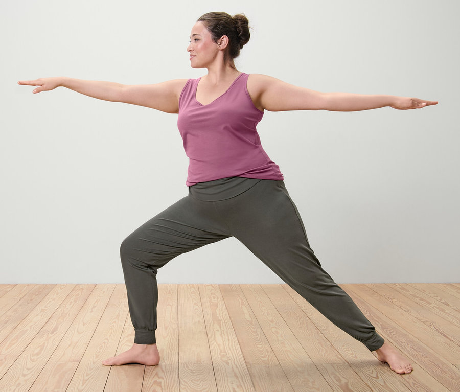 Femme en posture de guerrier portant un des deux tops mauve et un pantalon de yoga.