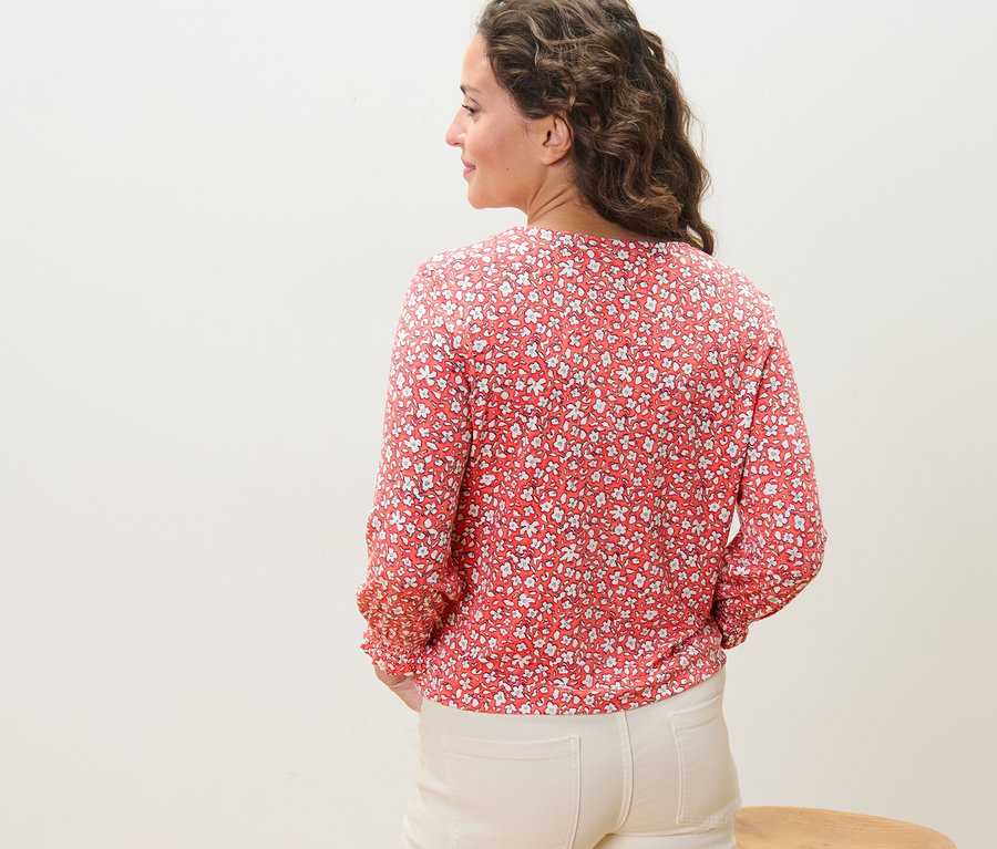Une femme, vue de dos, porte une blouse imprimée corail.