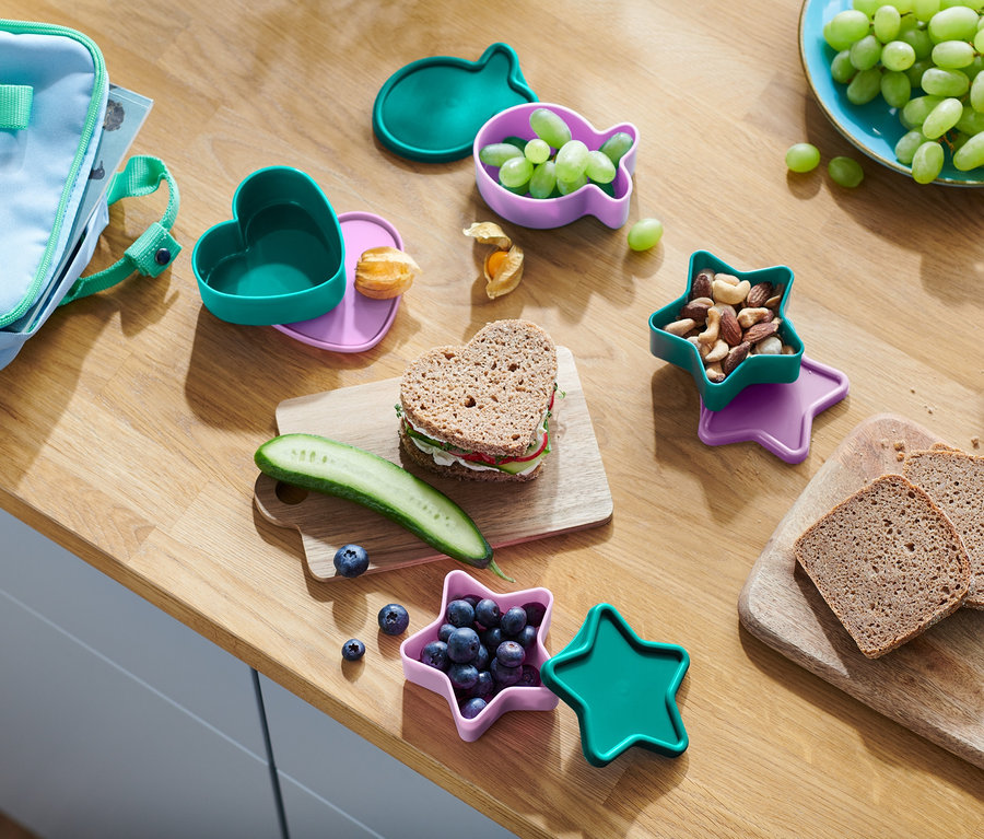 Sur une table en bois, il y a une collation. Sandwich en forme de cœur, concombre, myrtilles dans un récipient en forme d'étoile, noix, raisins dans un récipient en forme de poisson et pain.