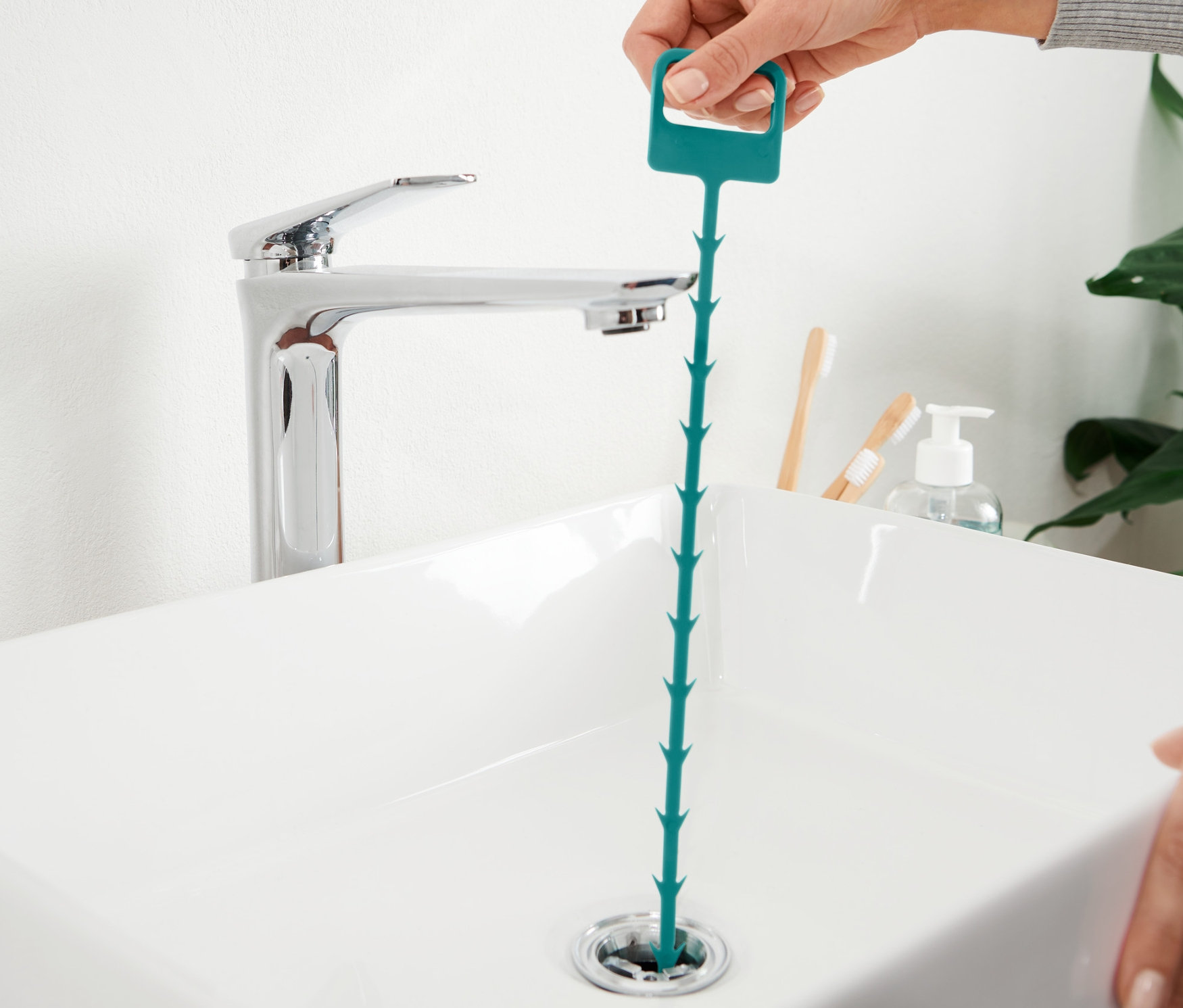 Une main insère une tige de curage dans le drain d'un lavabo.