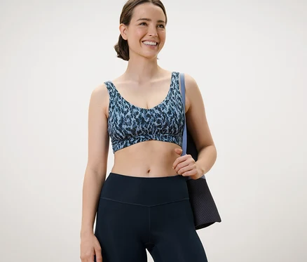 Une femme porte une brassière de sport à imprimé intégral et tient un tapis d'entraînement.